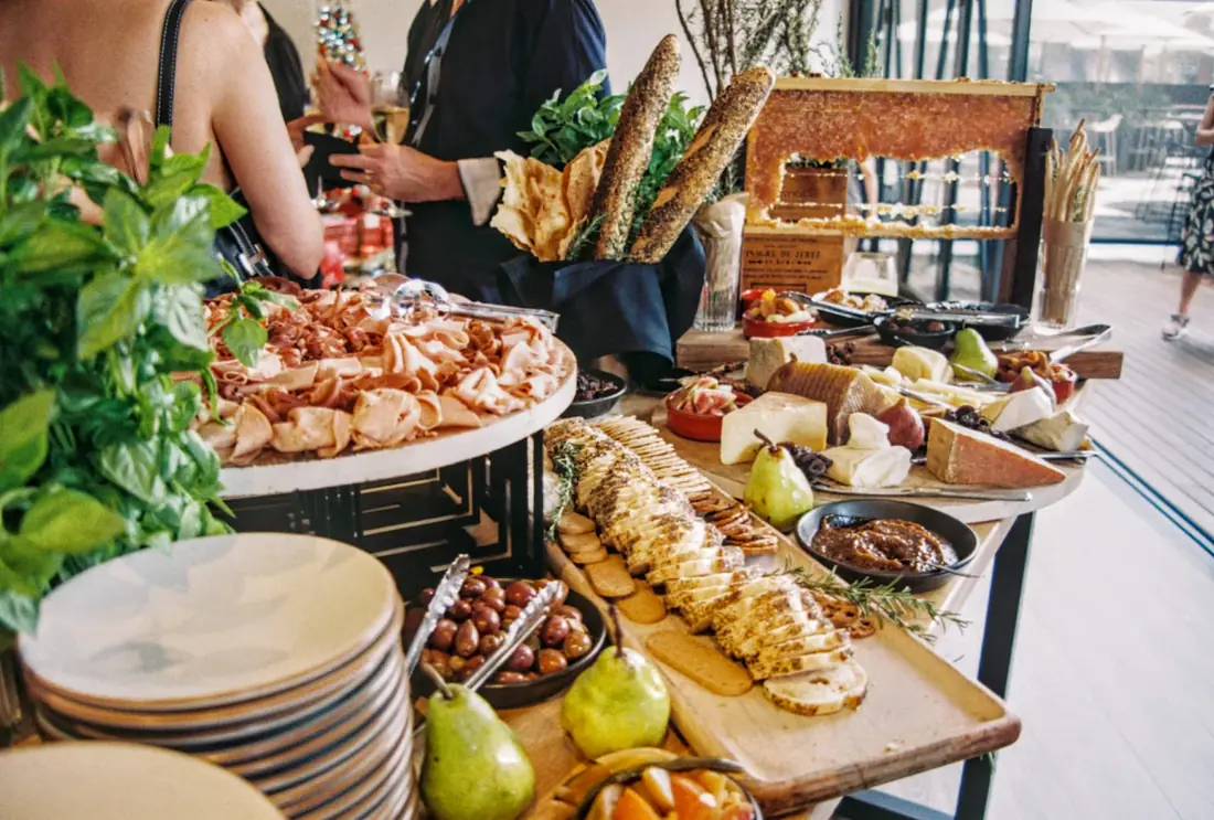 A buffet line with stacked plates, grilled vegetables and fruit