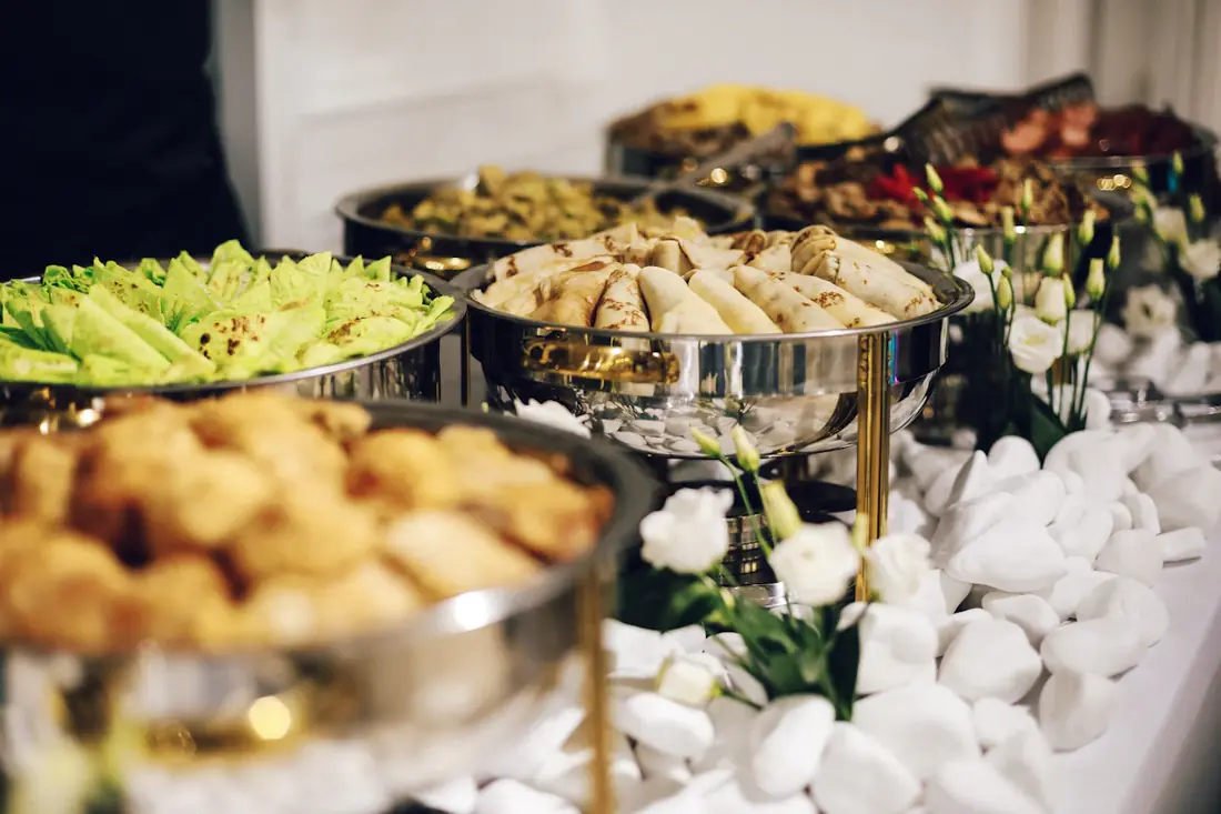 A catered spread of fried bites, salads and pastries in silver trays